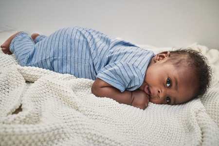 Baby lying on a knitted blanket wearing a blue striped outfit