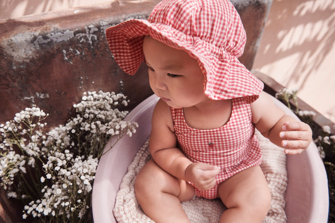 Baby wearing a red outfit and sun hat sitting outdoors