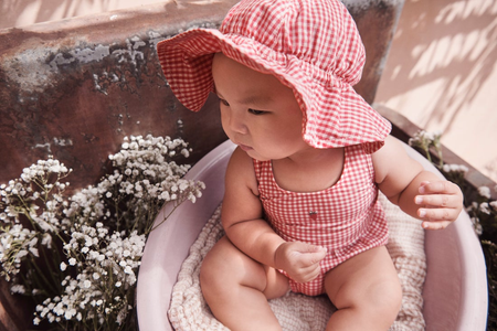 Baby wearing a red outfit and sun hat sitting outdoors