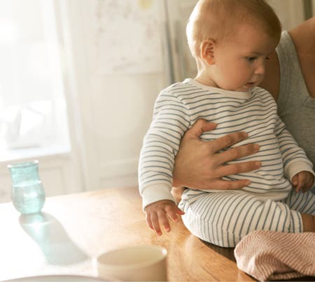 baby held by mother seated by dining table in daydream fleece striped shirt and pants