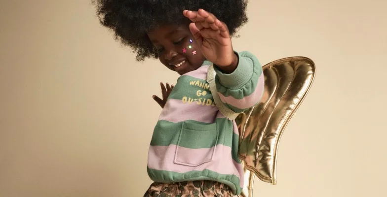 toddler girl in striped sweatshirt and gold play wings